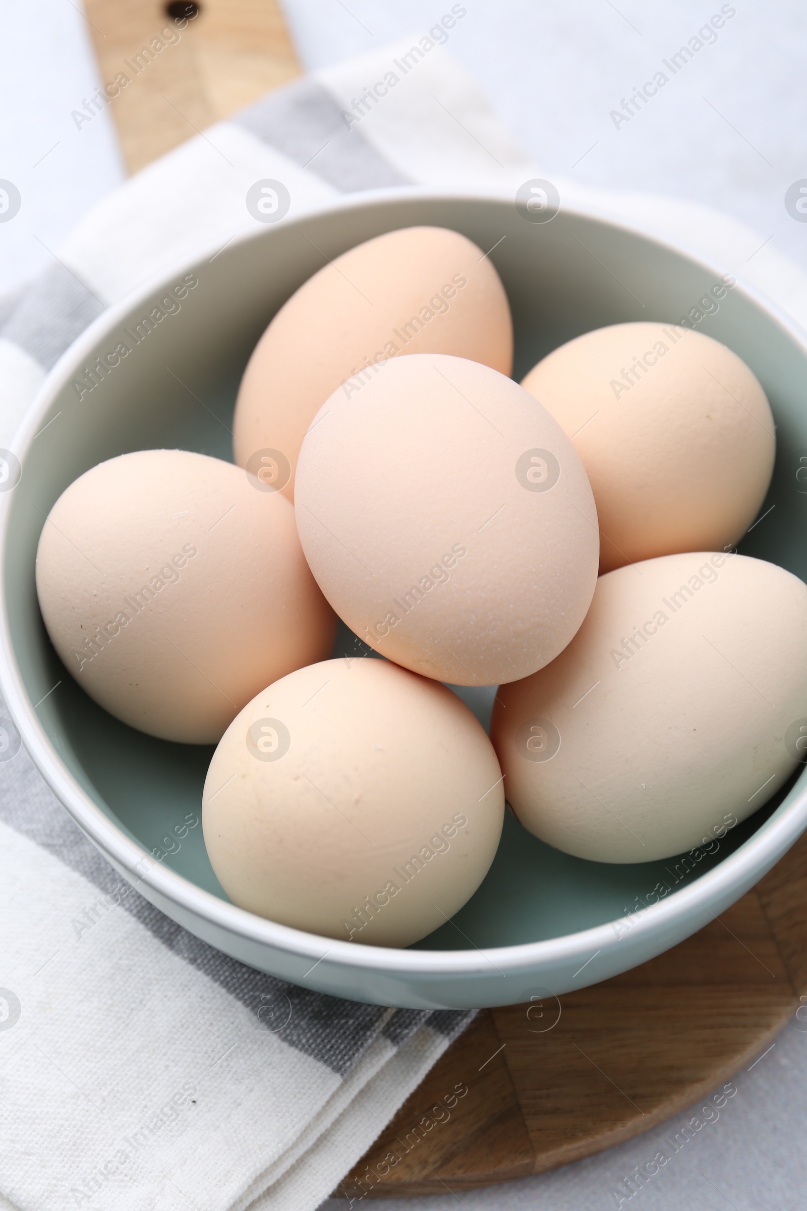 Photo of Raw chicken eggs in bowl on white table, closeup