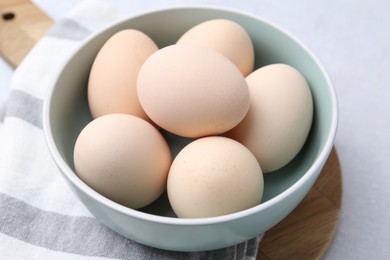 Photo of Raw chicken eggs in bowl on white table, closeup