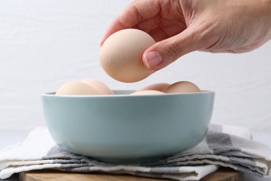 Photo of Woman taking raw chicken egg from bowl at table, closeup