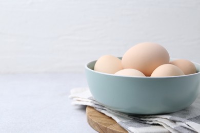 Photo of Raw chicken eggs in bowl on white table, closeup. Space for text