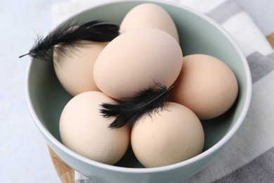Photo of Raw chicken eggs and feathers in bowl on white table, closeup