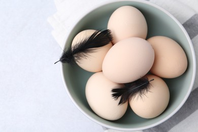 Photo of Raw chicken eggs and feathers in bowl on white table, top view. Space for text