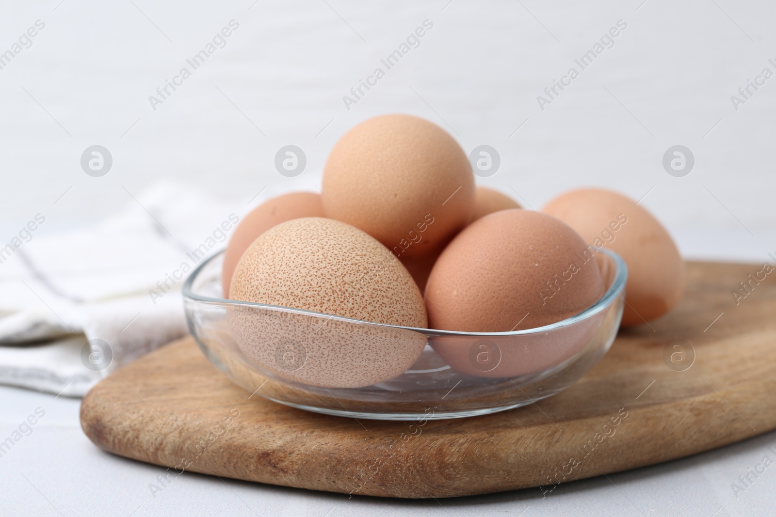 Photo of Raw chicken eggs in bowl on white table, closeup