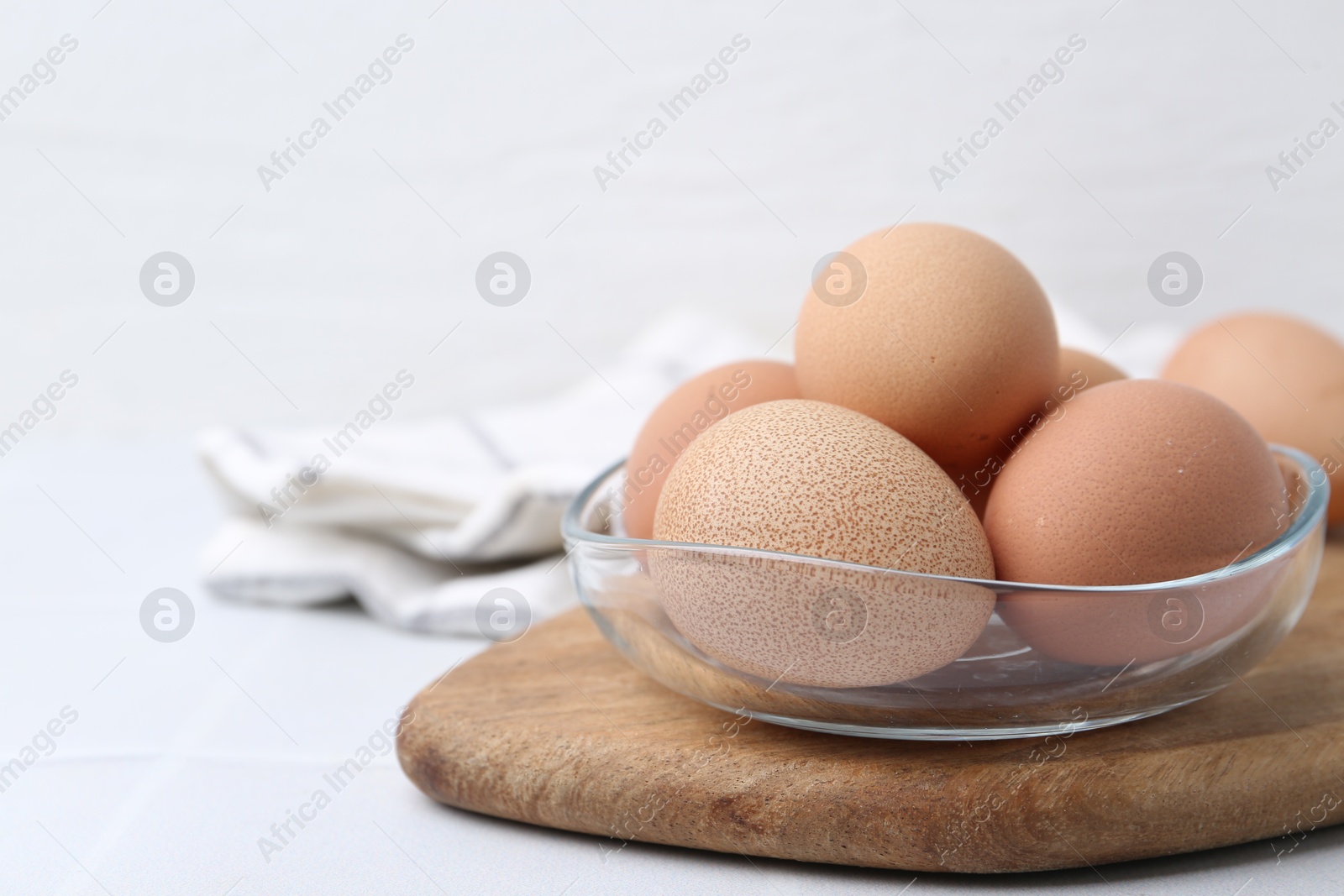 Photo of Raw chicken eggs in bowl on white tiled table, closeup. Space for text
