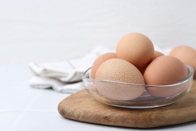 Photo of Raw chicken eggs in bowl on white tiled table, closeup. Space for text