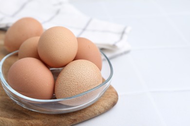 Photo of Raw chicken eggs in bowl on white tiled table, closeup. Space for text