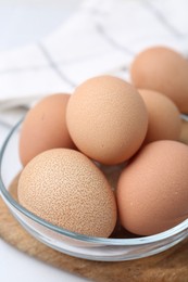 Photo of Raw chicken eggs in bowl on white table, closeup