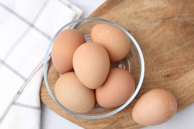 Photo of Raw chicken eggs in bowl on white table, top view