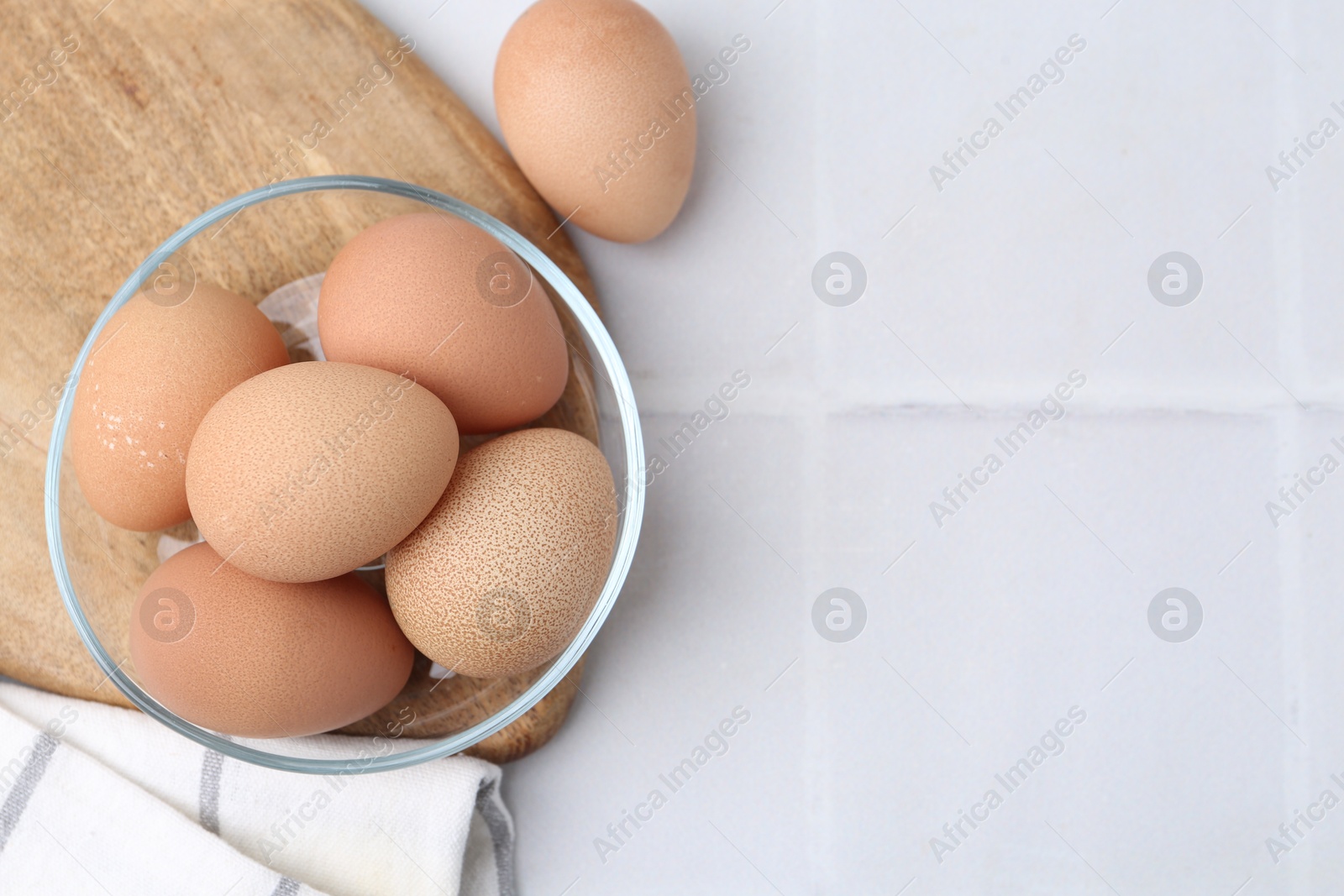 Photo of Raw chicken eggs in bowl on white tiled table, top view. Space for text