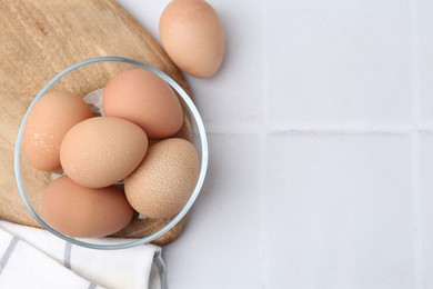 Photo of Raw chicken eggs in bowl on white tiled table, top view. Space for text