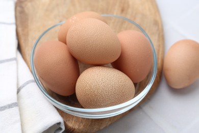 Photo of Raw chicken eggs in bowl on white tiled table, closeup