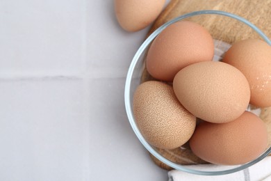 Photo of Raw chicken eggs in bowl on white tiled table, top view. Space for text