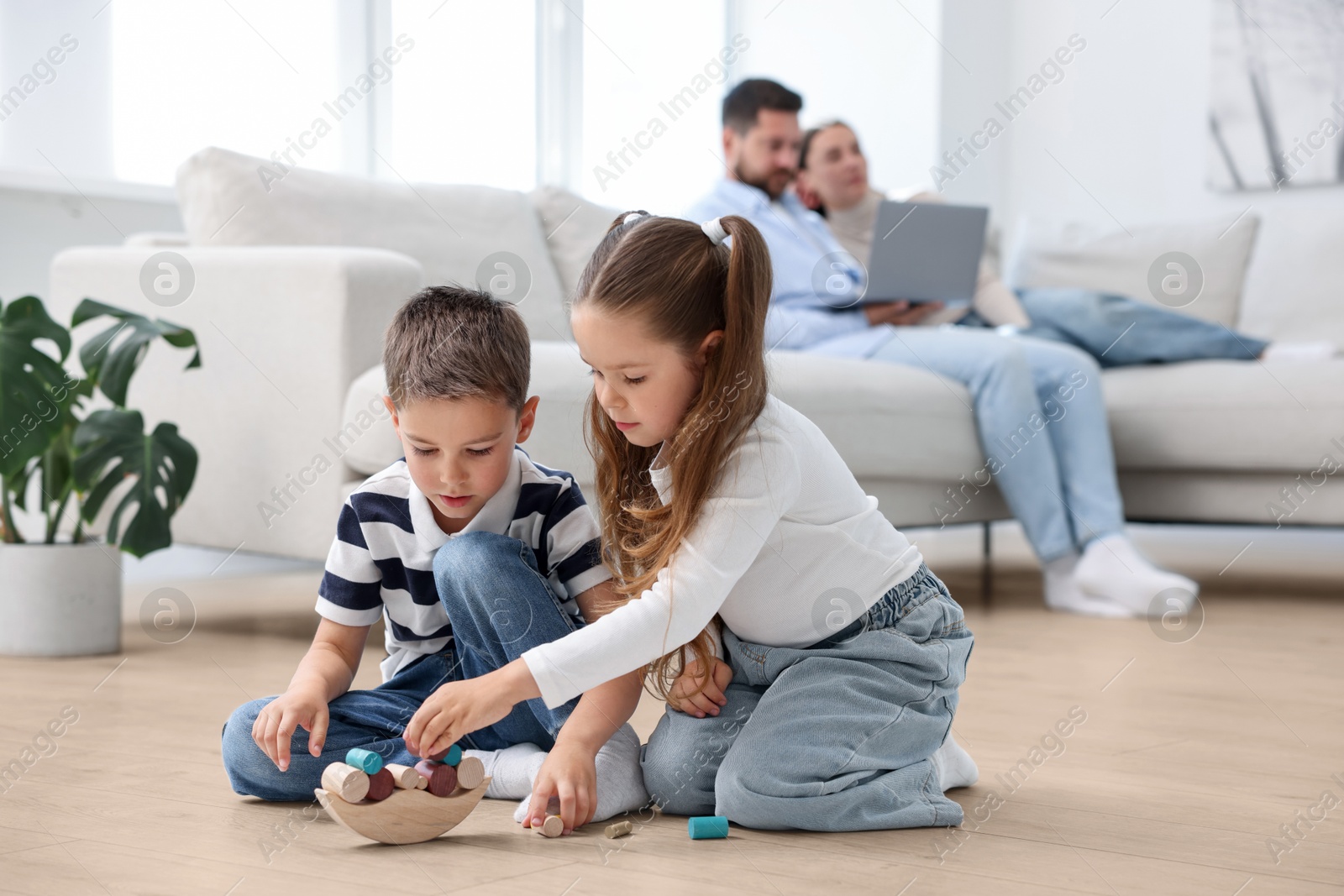 Image of Children feeling comfortable on warm floor, while their parents sitting on sofa at home. Underfloor heating