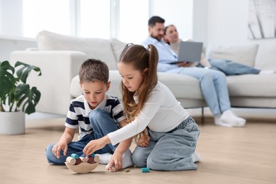 Image of Children feeling comfortable on warm floor, while their parents sitting on sofa at home. Underfloor heating