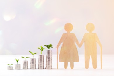 Image of Retirement savings. Stacked coins with green sprouts on tops and wooden figure of two old people on table