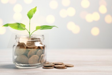 Image of Jar with coins and green sprout on white table against blurred lights. Savings concept