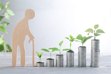 Image of Retirement savings. Stacked coins with green sprouts on tops and wooden figure of old man on table