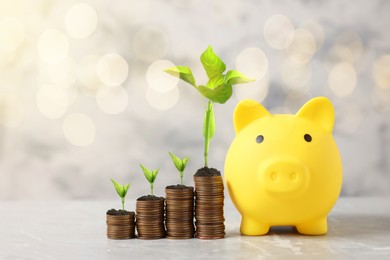 Image of Savings concept. Stacked coins with green sprouts on tops and piggy bank on table, bokeh effect