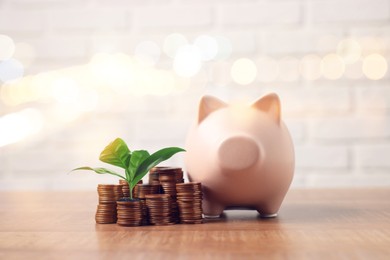 Image of Savings concept. Stacked coins, green sprout and piggy bank on table, bokeh effect