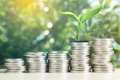 Image of Savings concept. Stacked coins and green sprout on table against blurred background