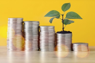 Image of Savings concept. Stacked coins and green sprout on table against orange background