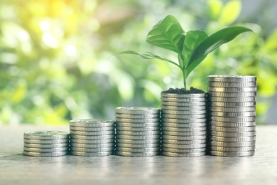 Image of Savings concept. Stacked coins and green sprout on table against blurred background
