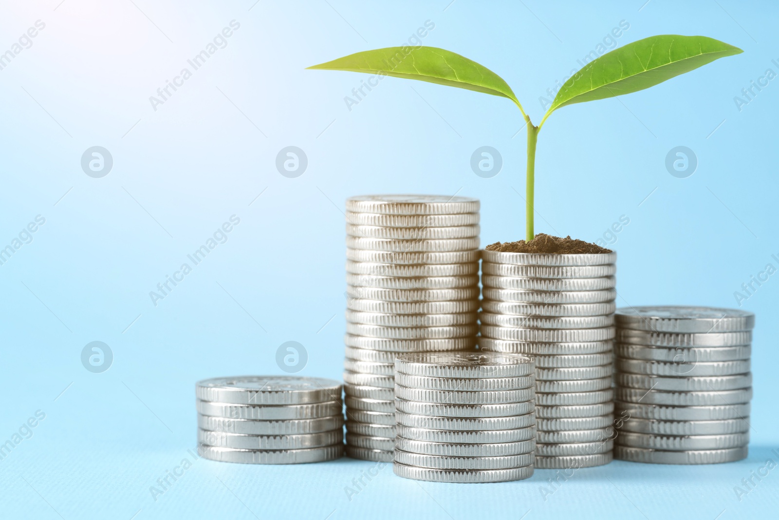 Savings concept. Stacked coins and green sprout on light blue background Image of Savings concept. Stacked coins and green sprout on light blue background