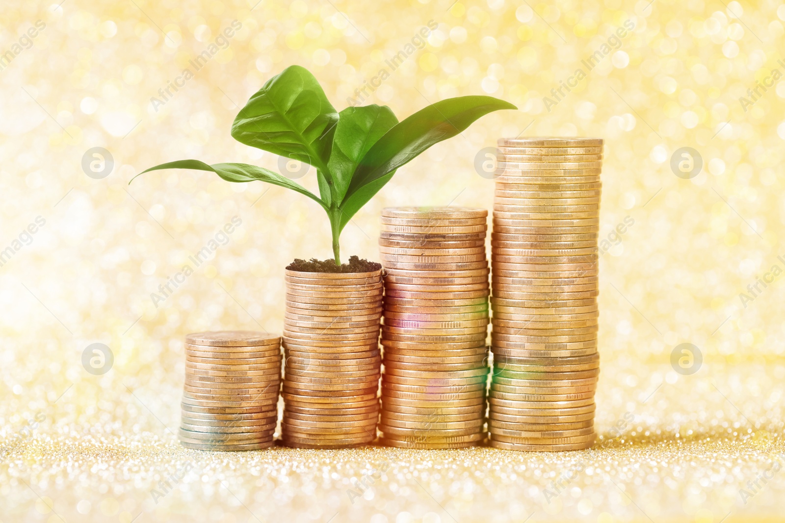 Savings concept. Stacked coins and green sprout on shiny golden background Image of Savings concept. Stacked coins and green sprout on shiny golden background