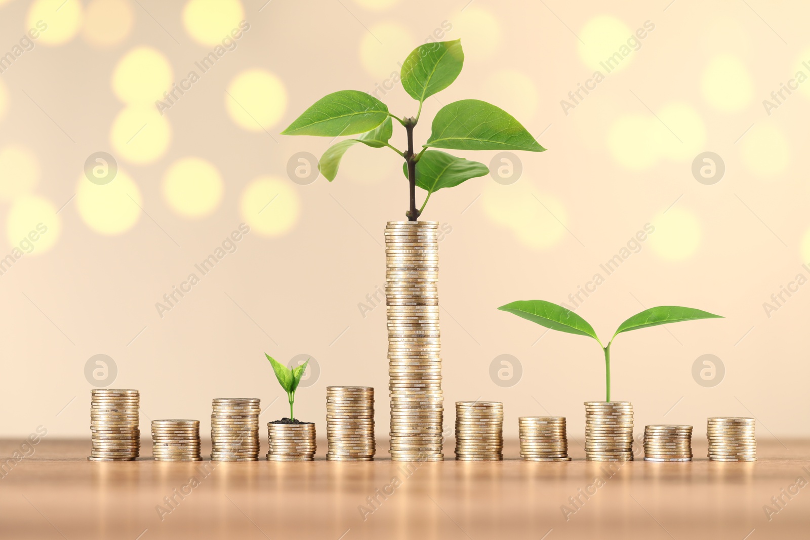 Savings concept. Stacked coins and green sprouts against beige background, bokeh effect Image of Savings concept. Stacked coins and green sprouts against beige background, bokeh effect