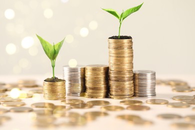 Image of Savings concept. Stacked coins and green sprouts against beige background, bokeh effect