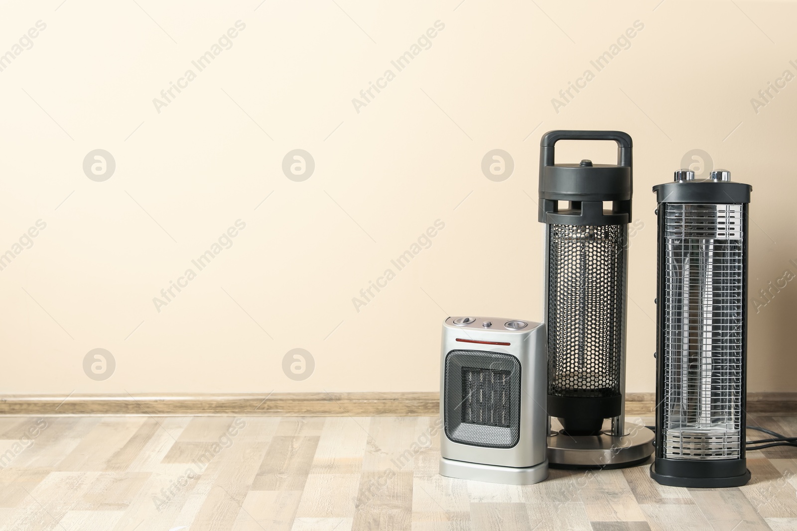 Different modern electric heaters on floor in room, space for text Photo of Different modern electric heaters on floor in room, space for text