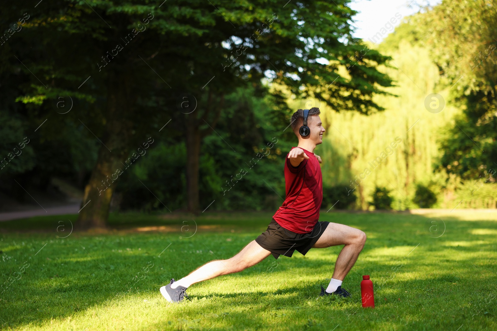 Photo of Smiling sportsman in headphones doing morning exercise outdoors