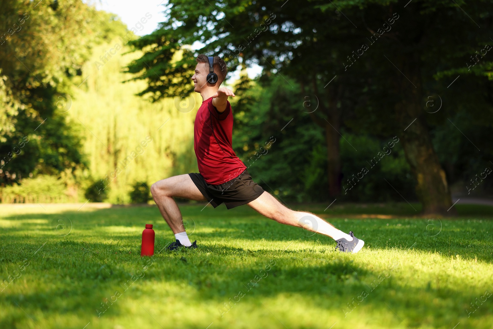 Photo of Smiling sportsman in headphones doing morning exercise outdoors