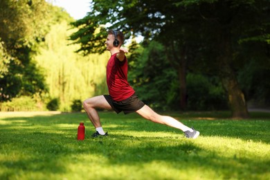 Photo of Smiling sportsman in headphones doing morning exercise outdoors