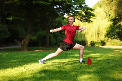 Photo of Smiling sportsman in headphones doing morning exercise outdoors
