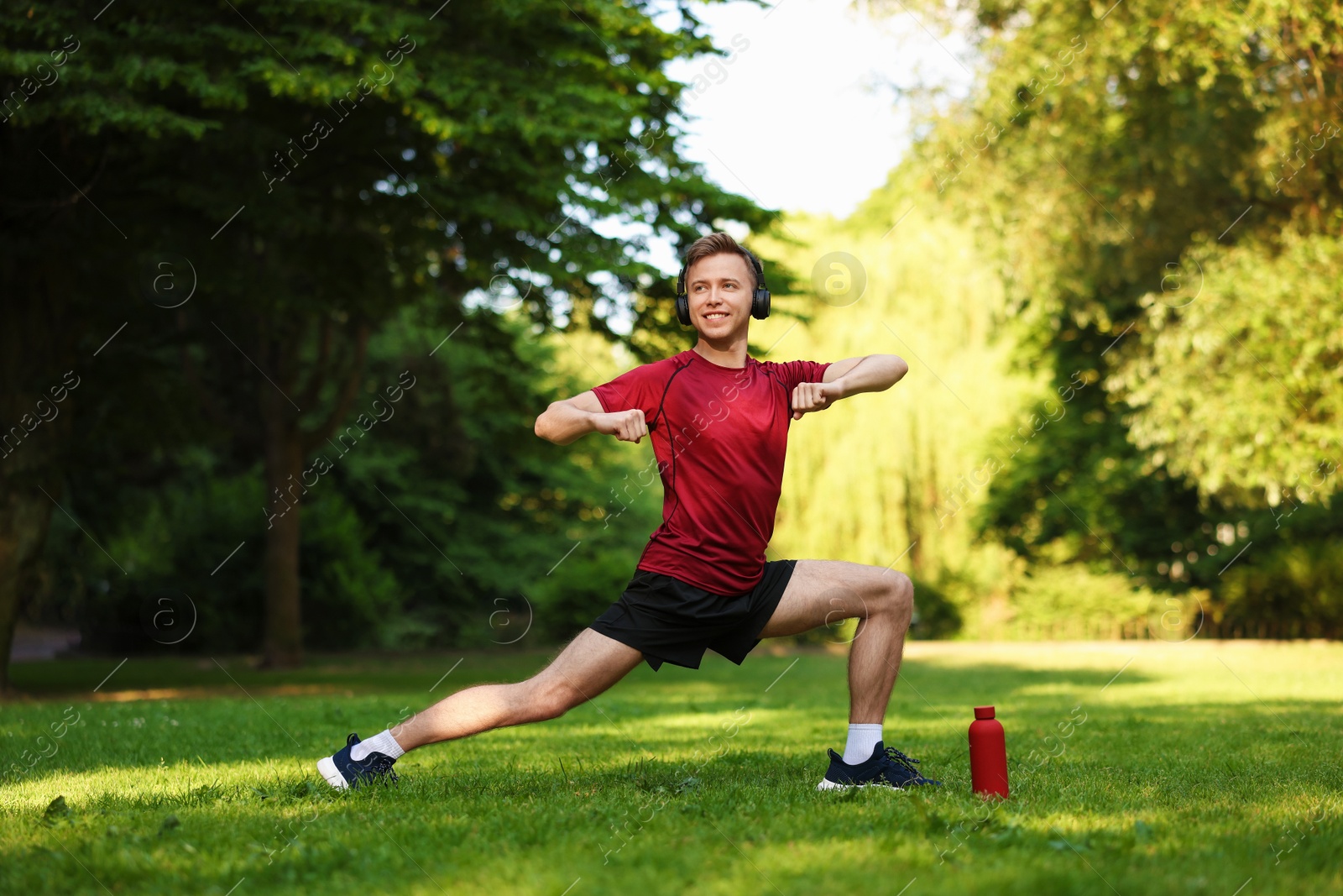 Photo of Smiling sportsman in headphones doing morning exercise outdoors