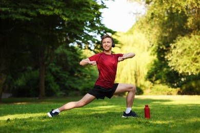 Photo of Smiling sportsman in headphones doing morning exercise outdoors