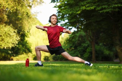 Photo of Smiling sportsman in headphones doing morning exercise outdoors