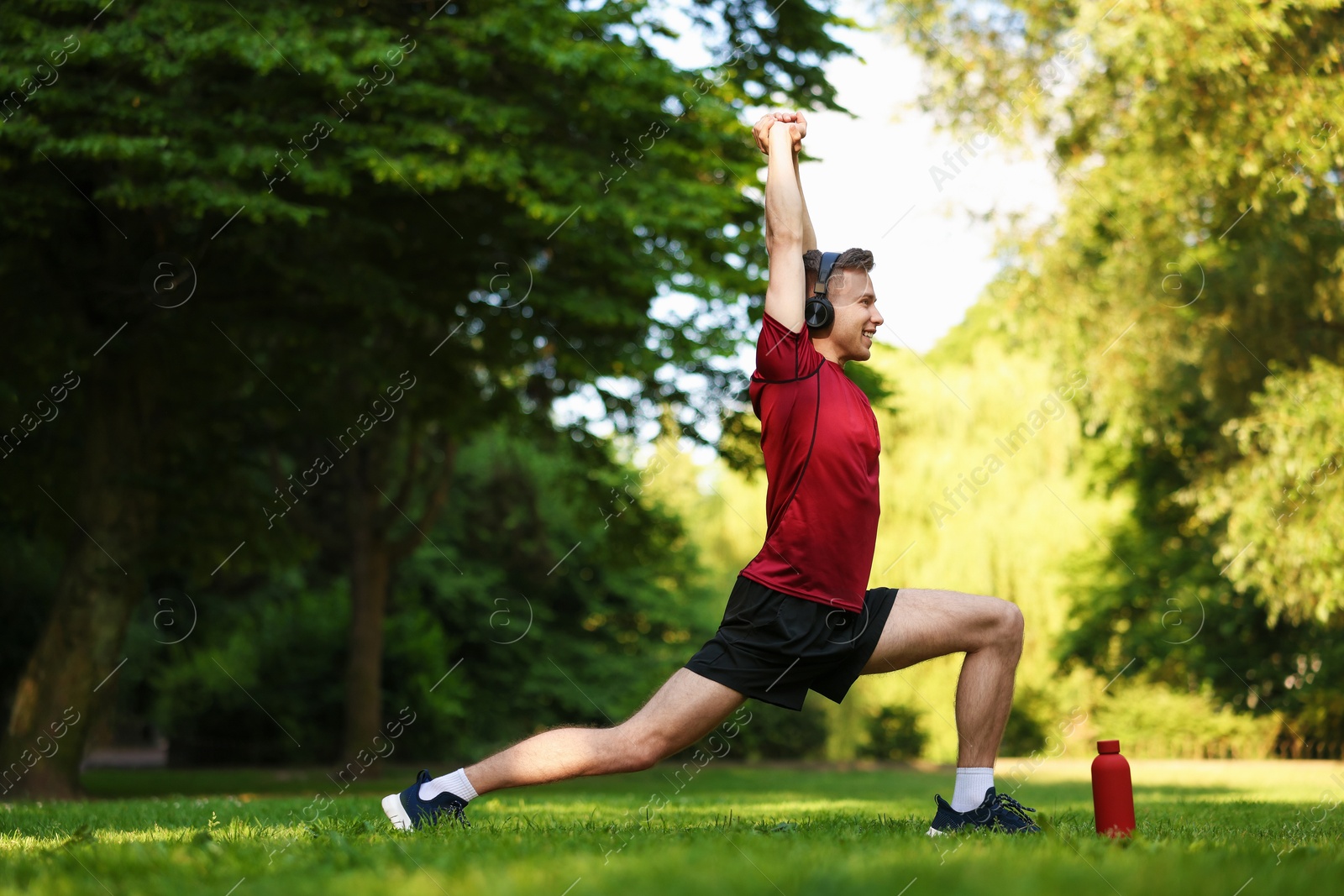 Photo of Smiling sportsman in headphones doing morning exercise outdoors
