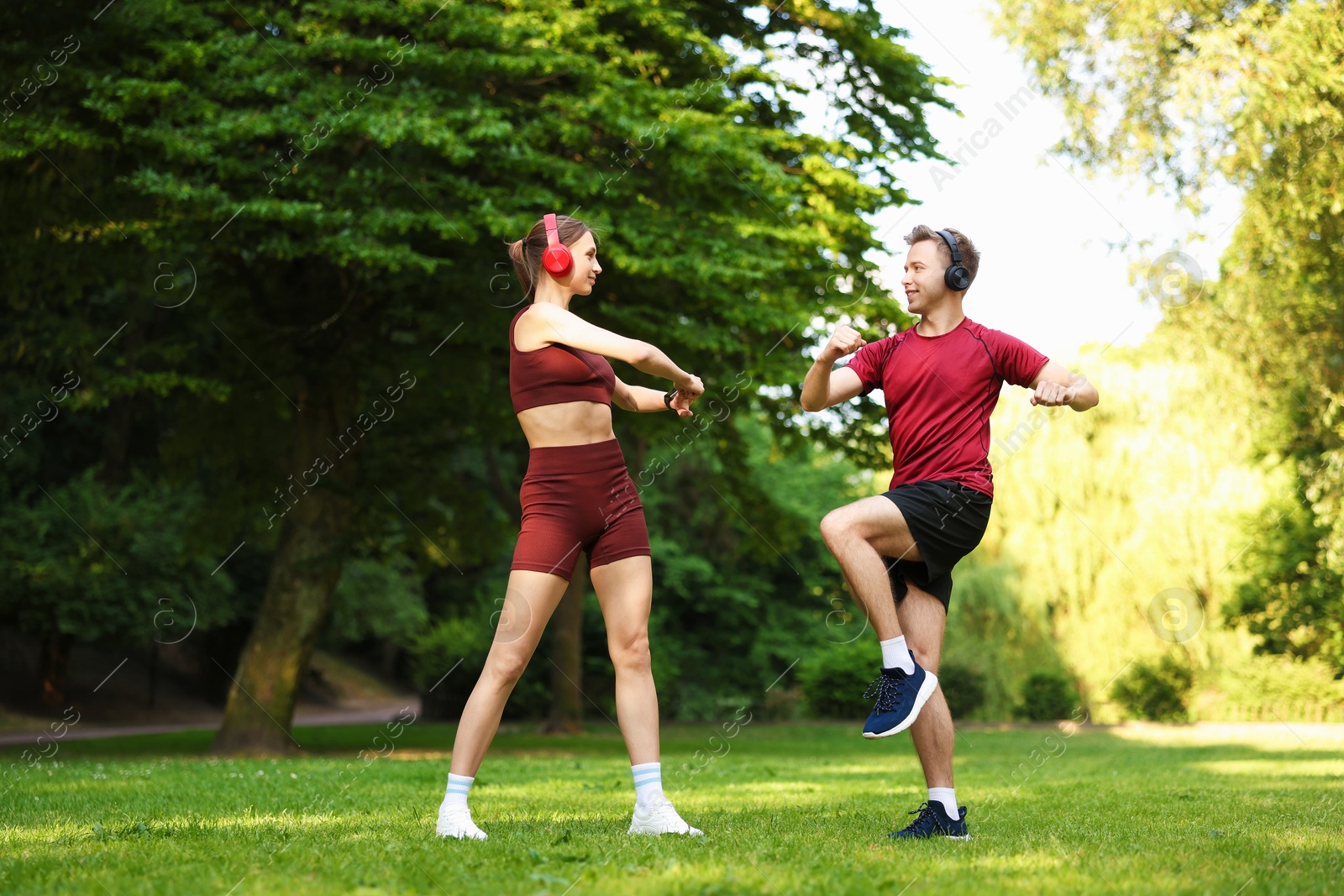 Photo of Happy couple in headphones doing morning exercises in park, low angle view