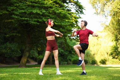 Photo of Happy couple in headphones doing morning exercises in park, low angle view