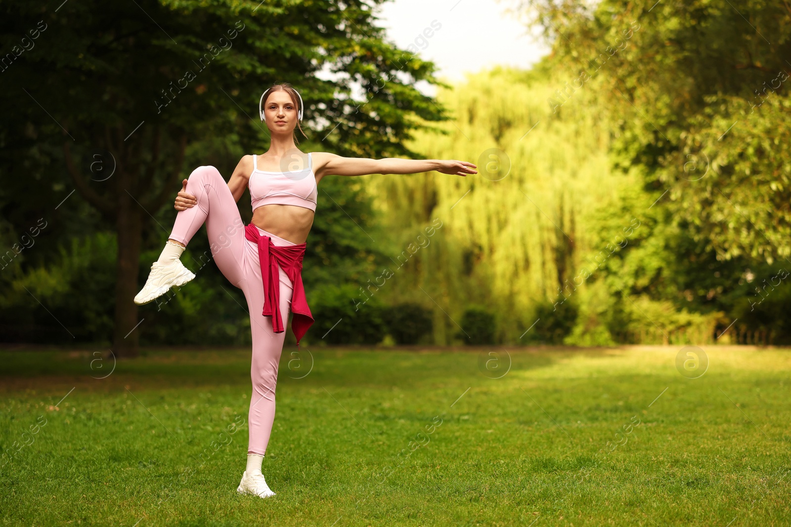 Photo of Young sportswoman in headphones doing morning exercise in park. Space for text