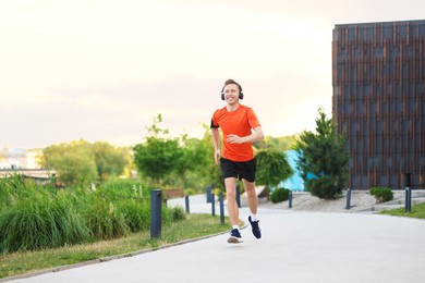 Photo of Smiling sportsman in headphones with armband running outdoors, low angle view. Morning exercise