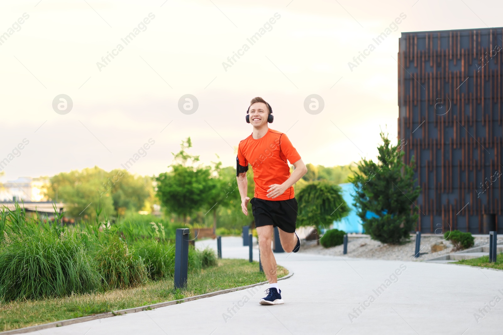 Photo of Smiling sportsman in headphones with armband running outdoors, low angle view. Morning exercise
