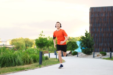 Photo of Smiling sportsman in headphones with armband running outdoors, low angle view. Morning exercise