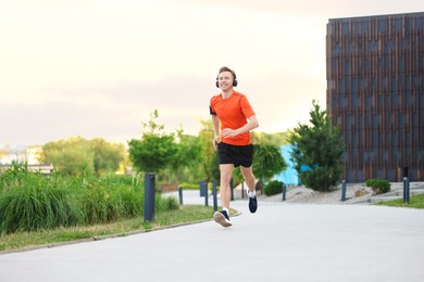 Photo of Smiling sportsman in headphones with armband running outdoors, low angle view. Morning exercise
