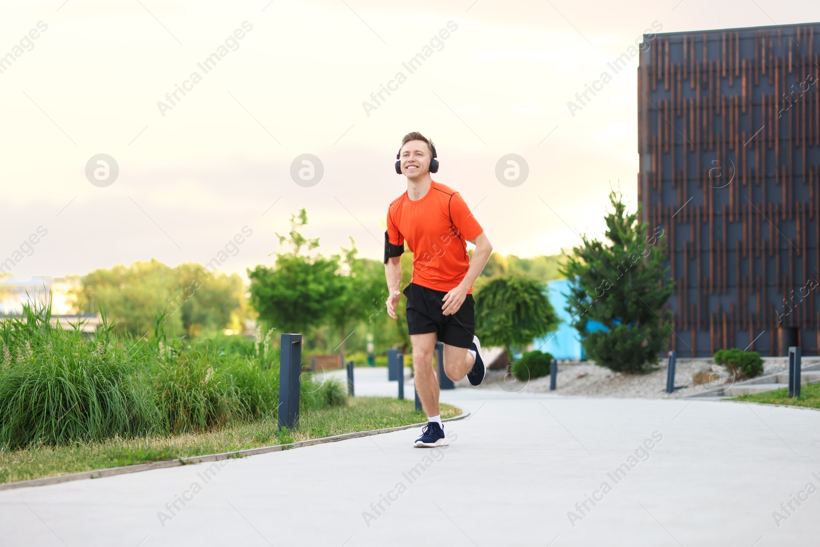 Photo of Smiling sportsman in headphones with armband running outdoors, low angle view. Morning exercise