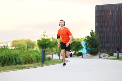 Photo of Smiling sportsman in headphones with armband running outdoors, low angle view. Morning exercise