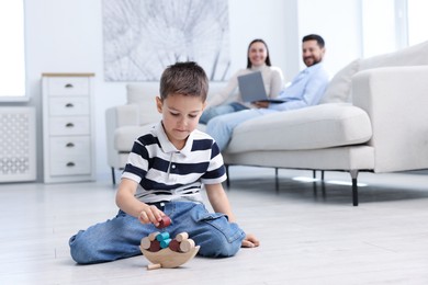 Photo of Boy playing with toys near his parents on warm floor at home, selective focus. Heating system