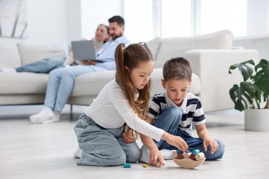 Photo of Kids playing with toys near their parents on warm floor at home, selective focus. Heating system